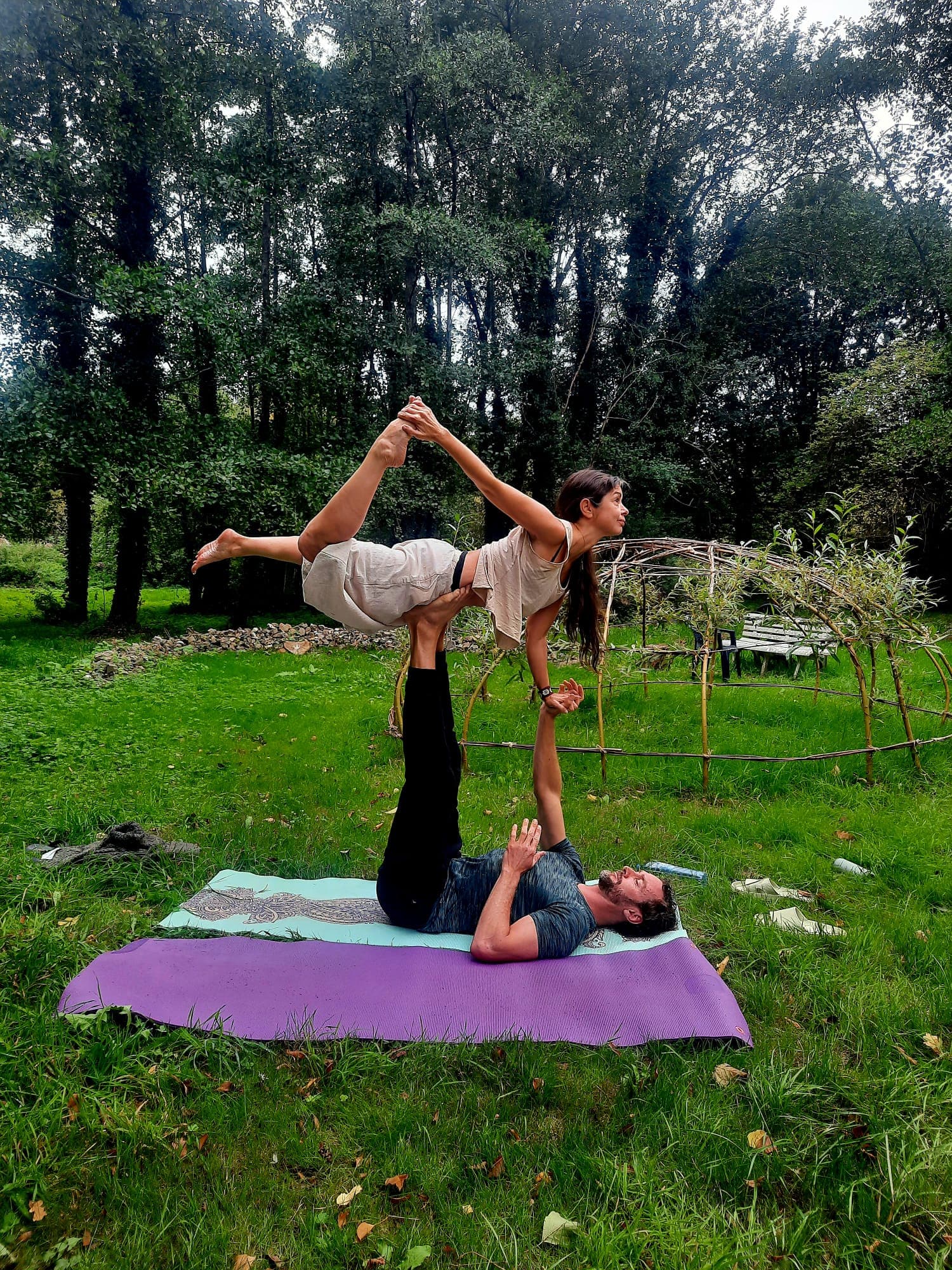Posture d'acro-yoga 'l'oiseau' (bird pose) effectuée en plein air sur l'herbe.